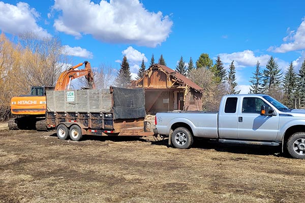 Excavator mid demolition of an old house with pickup truck parked in front